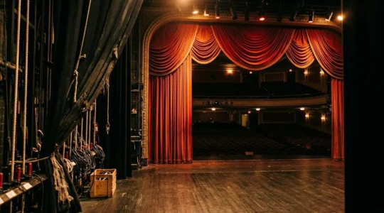 Vue depuis les coulisses d'une scène de théâtre vide baignée d'une lumière dramatique chaude avec des rideaux rouges en arrière-plan